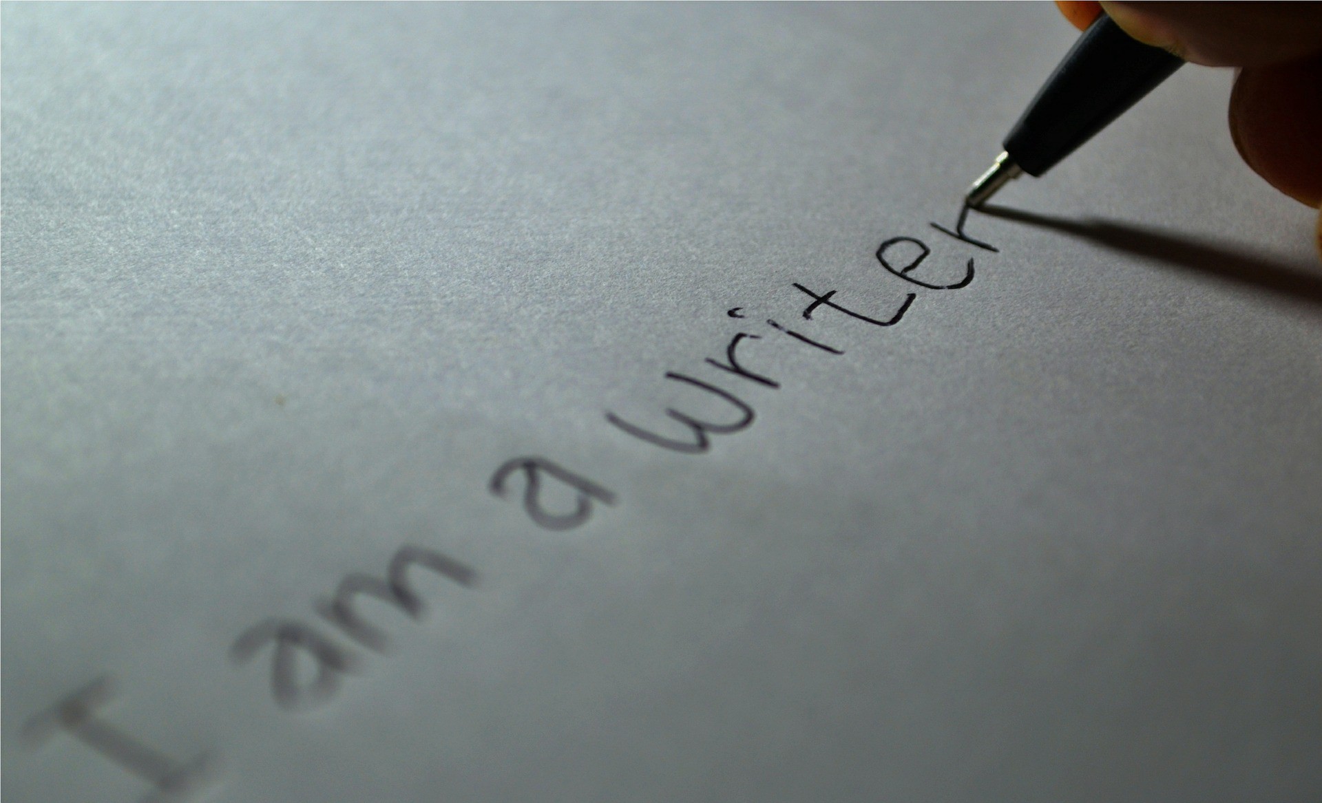 Person writing on a piece of paper with a pen. They're writing down, "I am a writer." 